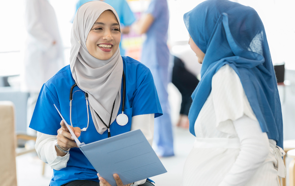 Smiling Malaysian ob/gyn reviews a pregnant woman's test results. Both women are wearing a hijab.